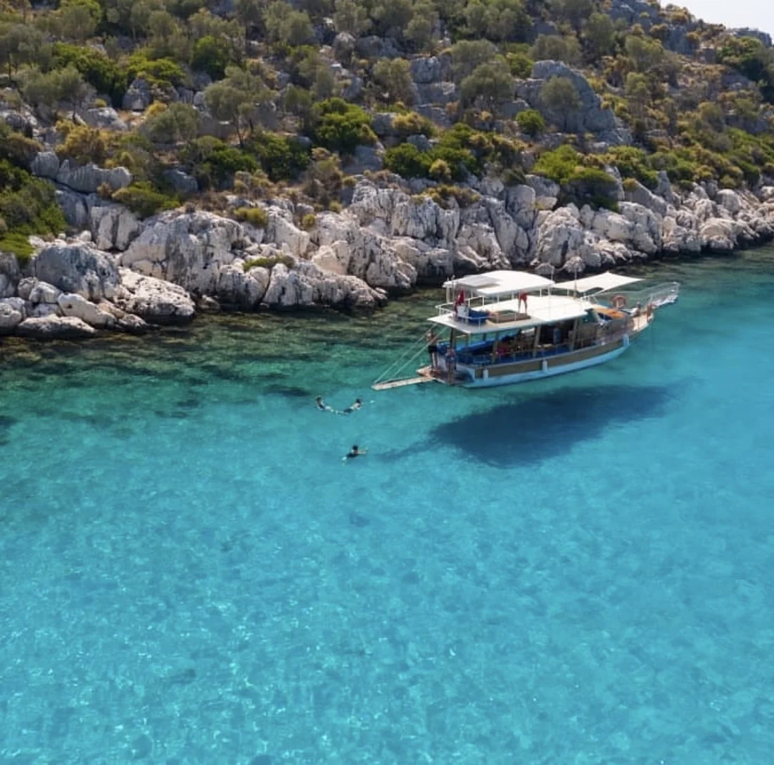 Ein Boot liegt dicht vor einer felsigen Küste im türkisfarbenen Wasser.